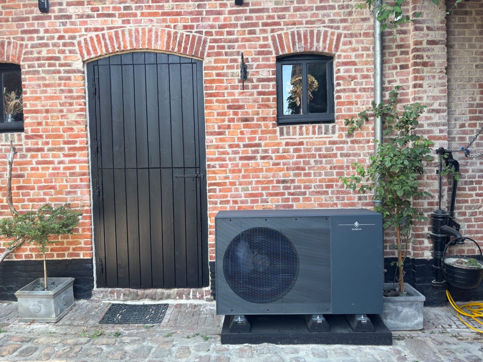 Pompe à chaleur air eau Bois-Grenier : groupe extérieur De Dietrich R290 devant la façade en brique de la dépendance