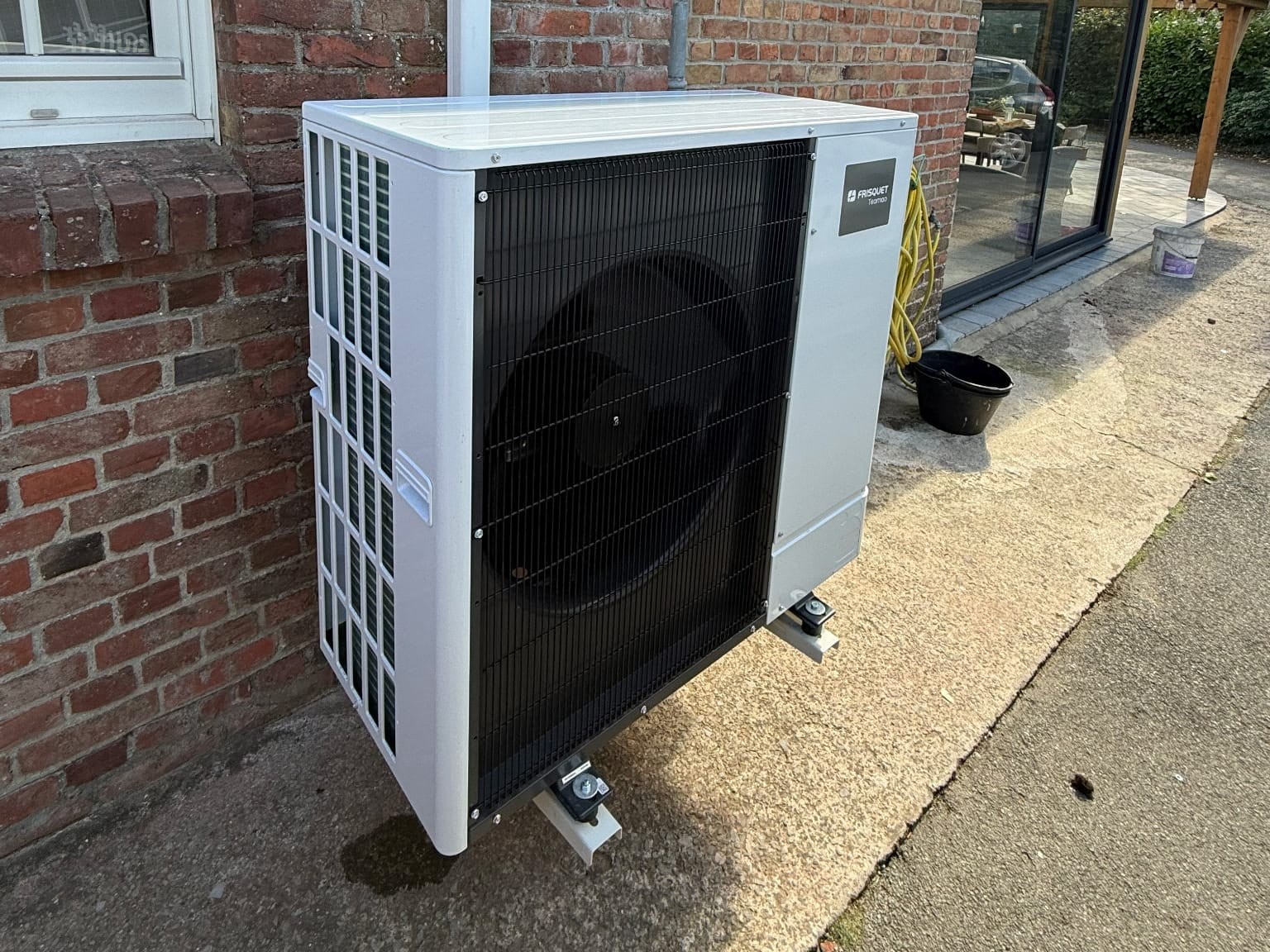 Pompe à chaleur air eau Steenwerck : groupe extérieur Frisquet Teamao sur support anti-vibratile contre un mur en brique